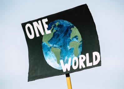 Protest sign with words One World and drawing of the Earth