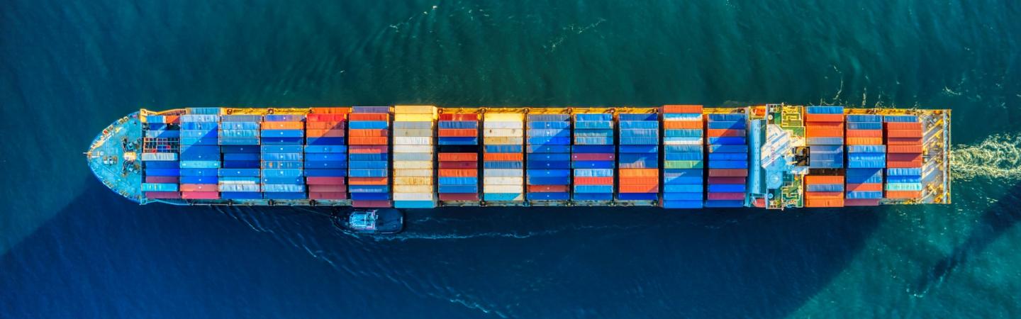 A large vessel full of shipping containers, viewed from above, crosses the water.