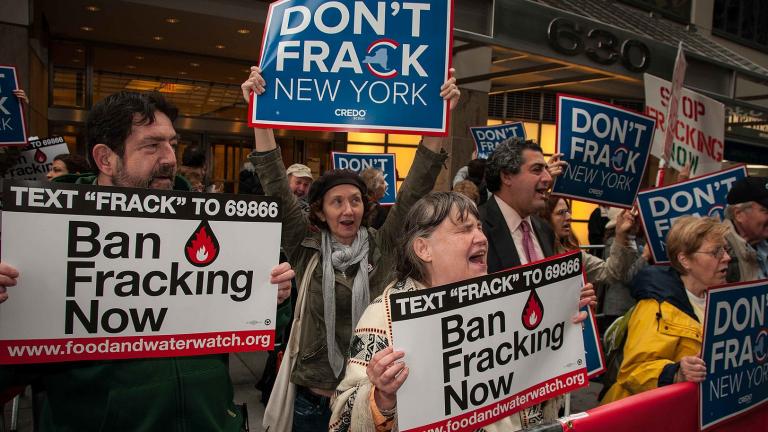 Photo of people chanting and holding signs reading "Ban Fracking Now."