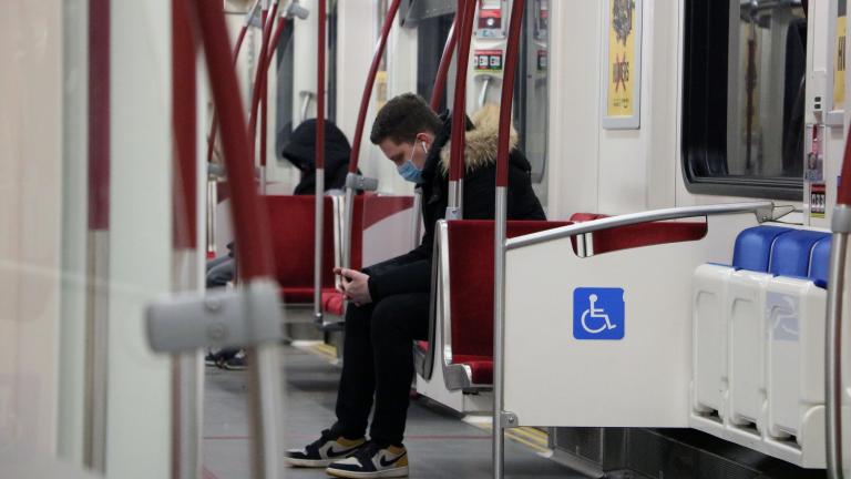 A man sits in a nearly-empty subway car, wearing a mask.