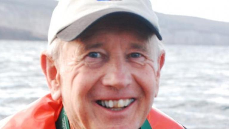 A portrait of Frederick Frey in an orange life vest standing in front of a stretch of water