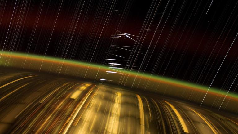 Captured by astronaut Don Pettit aboard the International Space Station (ISS), this long-exposure photograph showcases Earth's city lights, the upper atmosphere's airglow, and streaked stars. The bright flashes at the center are reflections of sunlight from SpaceX's Starlink satellites in low-Earth orbit.