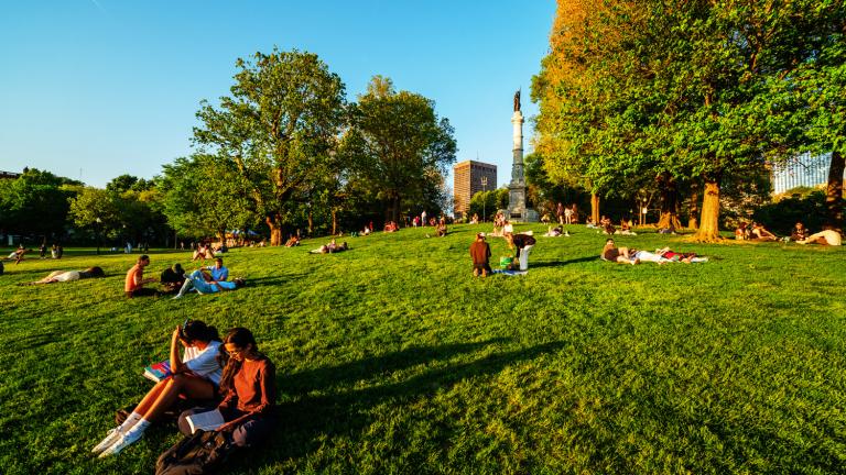People relax on the Boston Common lawn beneath the Soldiers and Sailors Monument.
