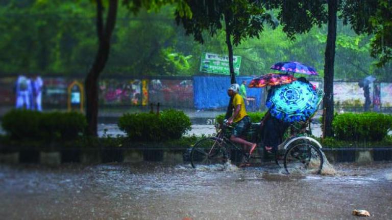 Man pedals rickshaw with passengers in heavy rain and flooded street