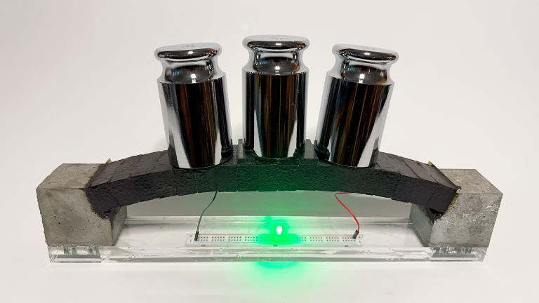 An electron-conducting carbon concrete (ec³)-based arch structure integrates supercapacitor electrodes for dual functionality. The prototype demonstrates both structural load bearing and the ability to power an LED, with the light’s intensity varying under applied load, highlighting the potential for real-time structural health monitoring via the supercapacitor.