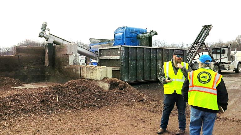Two people stand in front of a large machine at a compost processing facility in Maryland.