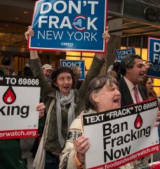 Photo of people chanting and holding signs reading "Ban Fracking Now."