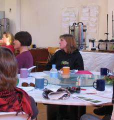 Photo of several students in a classroom sitting around a table, with instructor in the background.