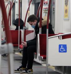 A man sits in a nearly-empty subway car, wearing a mask.