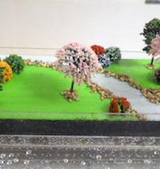 Photo of a diorama, with trees, grassy areas, and a stream, demonstrating water runoff and absorption.