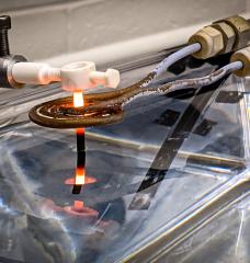 A thin rod of 3D-printed superalloy is drawn out of a water bath, and through an induction coil, where it is heated to temperatures that transform its microstructure, making the material more resilient. The new MIT heat treatment could be used to reinforce 3D-printed gas turbine blades.