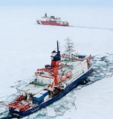 An icebreaker and Coast Guard cutter travel through a channel in the ice of the Arctic Ocean