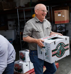A man laughs while carrying a white and green box that reads "farm fresh vegetables."
