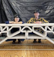 MIT Department of Civil and Environmental Engineering postdoc Hajin Kim-Tackowiak (left) and graduate student Zane Schemmer pose with the 3D-printed concrete bridge they designed and load-tested.