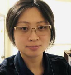 A portrait of Wanying Kang, in glasses and a collared black shirt, in an overexposed room.